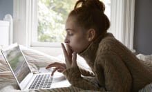 Teen girl looks at laptop computer while lying on her bed. 