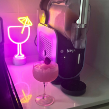 the ninja slushi on a countertop next to a frozen drink and a neon sign