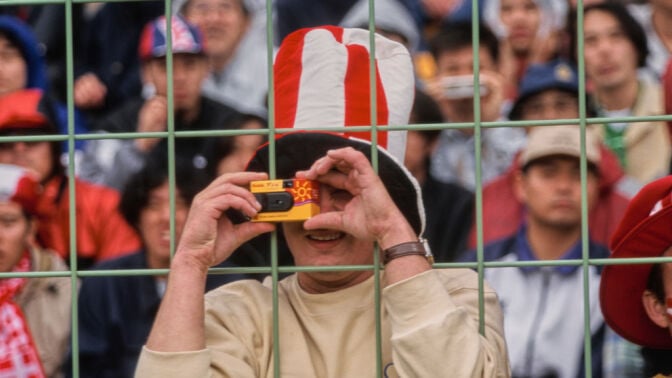 a male fan taking a photo with a kodak disposable camera at a soccer game