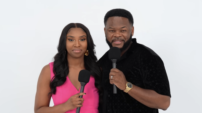 Black woman in pink oufit holding a microphone, standing next to Black man in black shirt