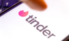 A finger points at Tinder logo on a smartphone screen.