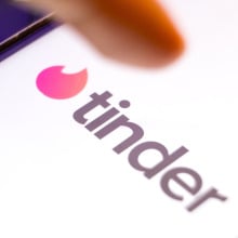 A finger points at Tinder logo on a smartphone screen.