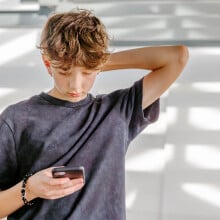 A teen boy looks down at his phone. 