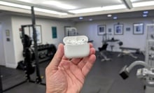 person holding airpods pr case in front of gym equipment