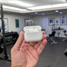 person holding airpods pr case in front of gym equipment