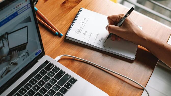 Pen writing on pad with laptop