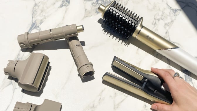 person holding base of shark glam over marble countertop where attachments are laid out