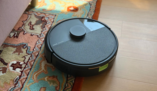 Roomba 105 robot vacuum cleaning rug near pink bed frame