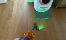 Leah sweeping up cat litter near automatic litter box with Dyson V12 Detect Slim vacuum