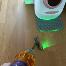 Leah sweeping up cat litter near automatic litter box with Dyson V12 Detect Slim vacuum