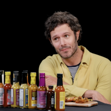 A man sits at a table covered in sauce bottles, a small smile on his face.