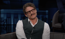 A man sits on a talk show chair, smiling.