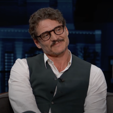 A man sits on a talk show chair, smiling.