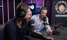 Two men sitting in a radio studio laugh.