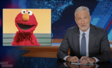 Jon Stewart presents a segment of the Daily Show beside a picture of Elmo.