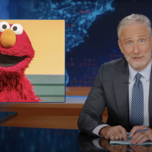 Jon Stewart presents a segment of the Daily Show beside a picture of Elmo.
