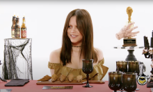 A woman sits at a table with wings in front of her and dark goblets.