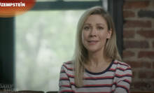 A woman sits on a sofa looking at the camera.
