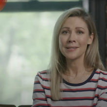 A woman sits on a sofa looking at the camera.