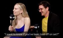 A man and a woman sit in a dark room with microphones, laughing. The caption reads, "I want to know if you've been told off on set?"