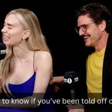 A man and a woman sit in a dark room with microphones, laughing. The caption reads, "I want to know if you've been told off on set?"