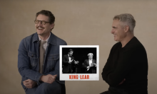 Two men sit on stools together, laughing.