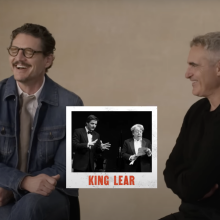 Two men sit on stools together, laughing.