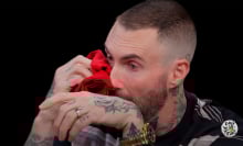 A man sits in a dark studio dabbing his eyes with a red napkin.