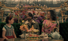 A little girl sits at a table with a man and a woman.