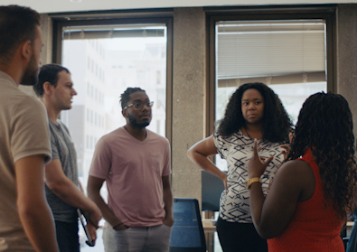 five people standing in a circle talking, two backs are to the camera